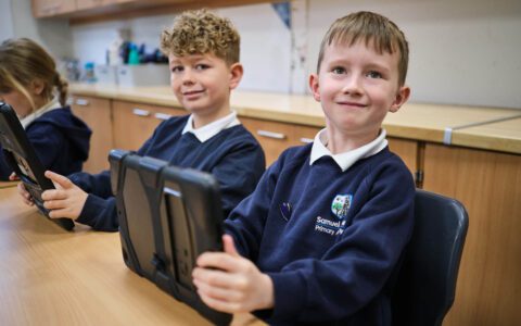 Two young boys sat at a desk with iPads